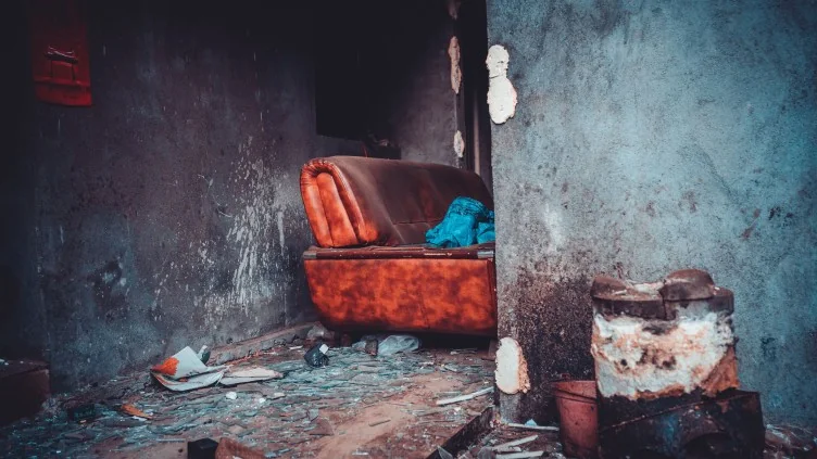 Interno di un’abitazione danneggiata, con macerie sul pavimento e una poltrona sullo sfondo